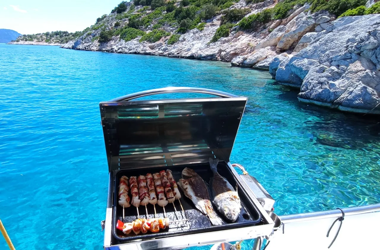 Fisch und Spieße auf einem Bootsgrill über klarem türkisfarbenem Wasser