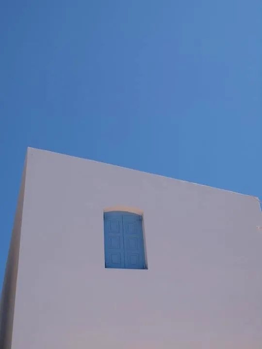 Eine weiß gekalkte Wand mit blauem Fenster vor tiefblauem Himmel auf Nisyros