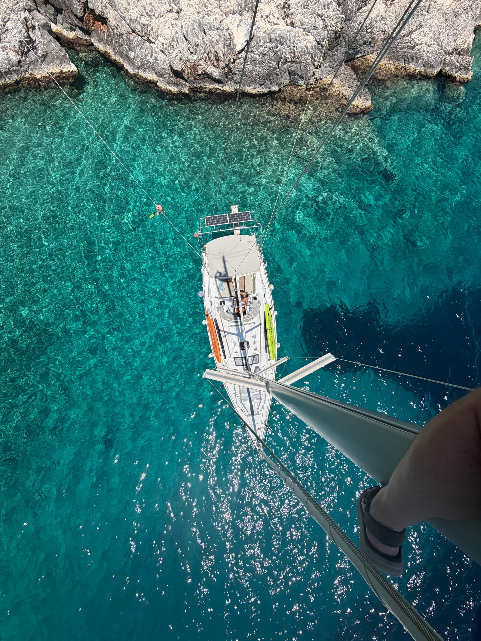 Ein Segelboot auf tiefblauem Wasser vor einer felsigen Küste, aus der Luft gesehen