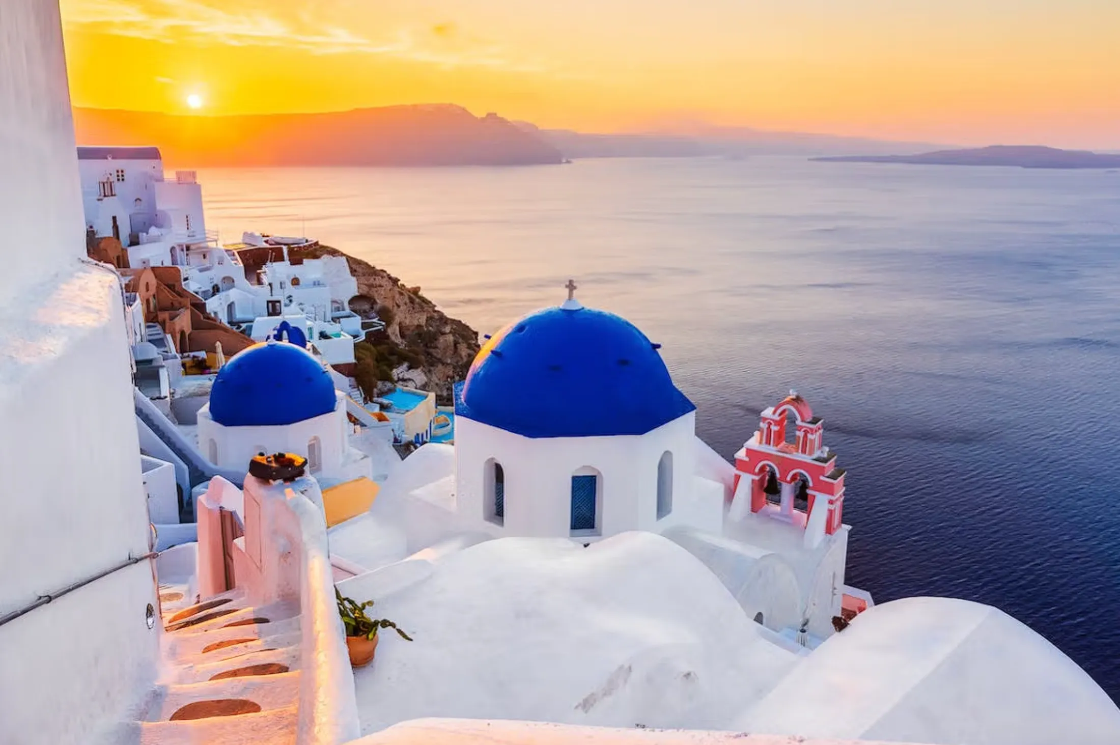 Oia bei Sonnenuntergang mit blauen Kuppeln über der Caldera