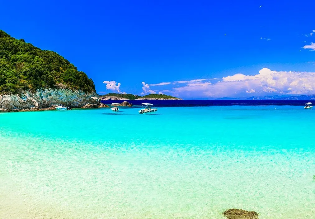 Der Strand von Voutoumi auf Antipaxos mit türkisfarbenem Wasser und kleinen Booten